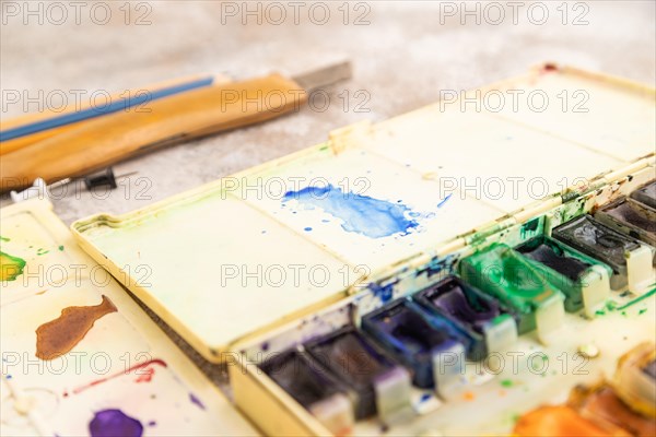 Drawing accessories set: brushes, pencils, watercolor on brown concrete background. Side view, close up, selective focus