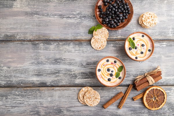 Yoghurt with bilberry and caramel in clay bowl on gray wooden background. top view, flat lay, copy space