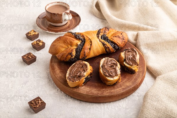 Homemade sweet bun with chocolate cream and cup of coffee on a gray concrete background and linen textile. side view, close up