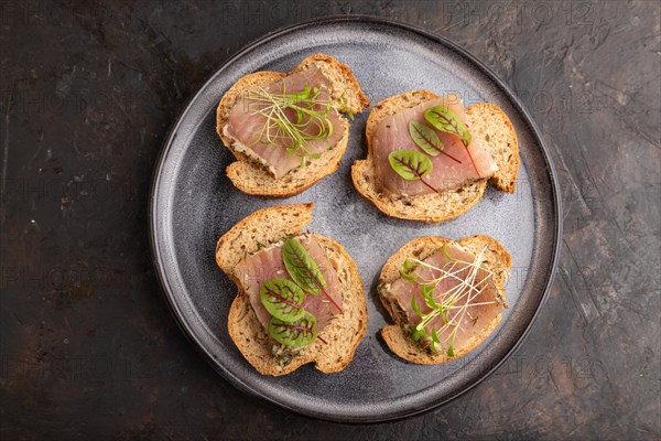 Bread sandwiches with jerky salted meat, sorrel and cilantro microgreen on black concrete background. top view, flat lay, close up