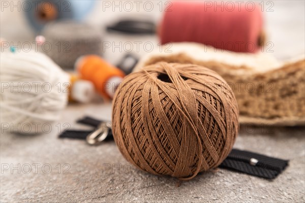 Sewing accessories: scissors, thread, thimbles, braid on brown concrete background. Side view, close up, selective focus