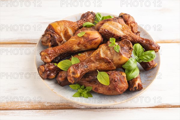 Smoked chicken legs with herbs and spices on a ceramic plate on a white wooden background. Side view, close up