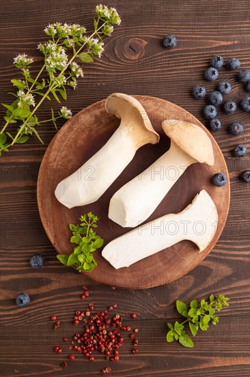 King Oyster mushrooms or Eringi (Pleurotus eryngii) on brown wooden background with blueberry, herbs and spices. Top view, flat lay