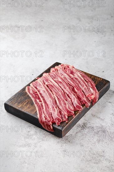 Fresh raw beef bacon strips on wooden cutting board