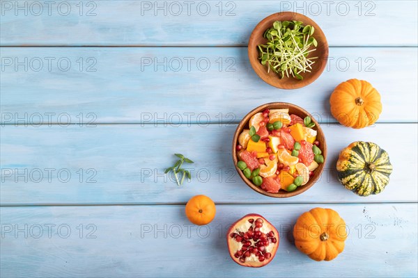 Vegetarian fruit salad of pumpkin, tangerine, pomegranate, grapefruit, sunflower microgreen sprouts on blue wooden background. Top view, flat lay, copy space