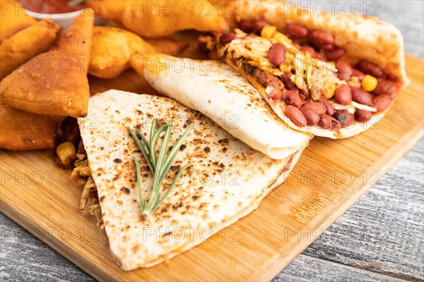 Set of snacks: nachos, chicken wings, fried ribs, bean tortillas on a cutting board on a gray wooden background. Side view, close up, selective focus