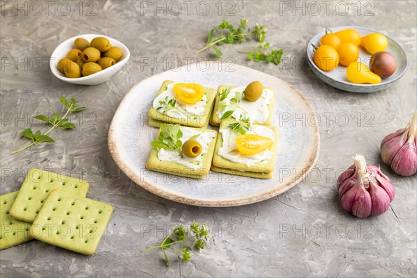 Green cracker sandwiches with cream cheese and cherry tomatoes on gray concrete background. side view, close up