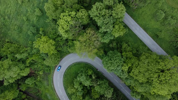 Blue car driving on serpentine road through green landscape, drone shot, Upper Bavaria, Bavaria, Germany, Europe