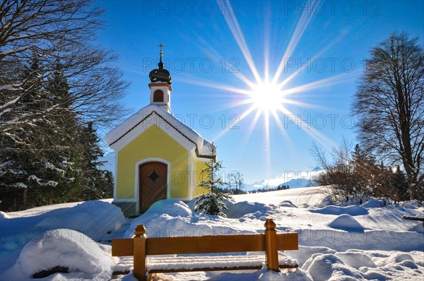 Backlit photograph of the snow-covered Maria Chapel on the humpback meadows of Werdenfelser Land near Garmisch in a wintry idyll, with the Karwendel Mountains in the background, Bavaria, Germany, Europe