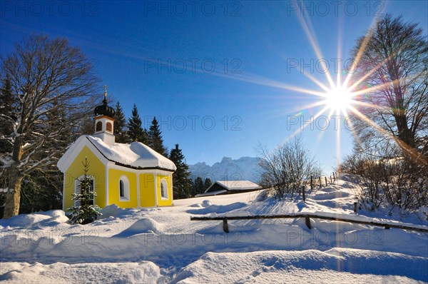 Backlit photograph of the snow-covered Maria Chapel on the humpback meadows of Werdenfelser Land near Garmisch in a wintry idyll, with the Karwendel Mountains in the background, Bavaria, Germany, Europe