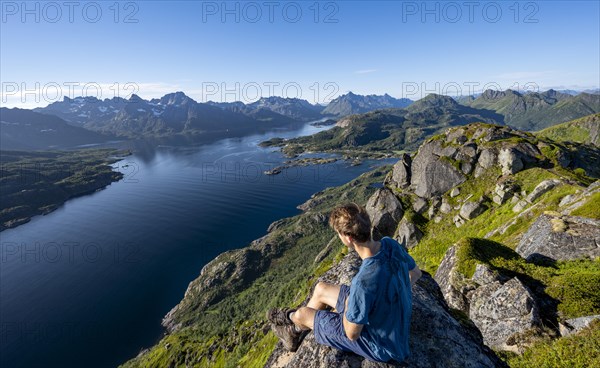Mountaineer sitting on the summit of Dronningsvarden or Stortinden, behind mountains and fjord Raftsund, Sonnenstern, Vesteralen, Norway, Europe