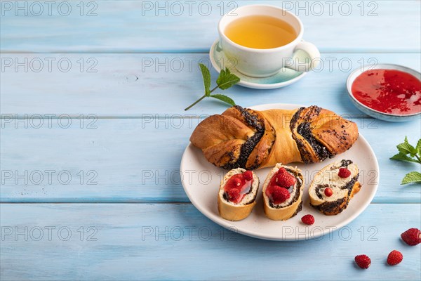 Homemade sweet bun with strawberry jam and cup of green tea on a blue wooden background. side view, copy space