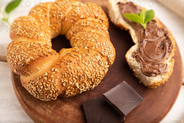 Homemade sweet bun with chocolate cream and cup of coffee on a white wooden background and linen textile. side view, close up, selective focus