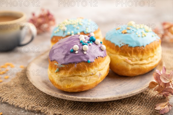 Purple and blue glazed donut and cup of coffee on brown concrete background and linen textile. side view, close up, selective focus. Breakfast, morning, concept