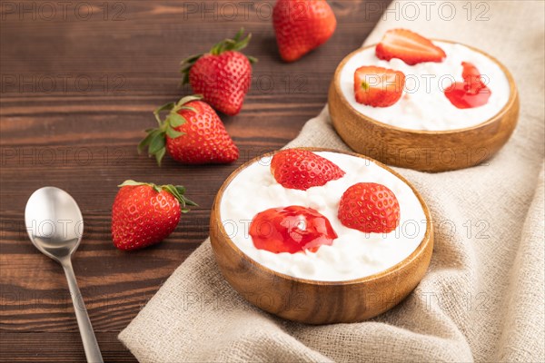 Grained cottage cheese with strawberry jam on brown wooden background and linen textile. side view, close up