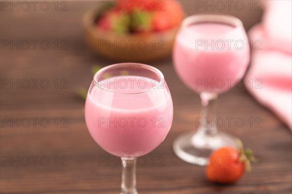 Sweet strawberry liqueur in glass on a brown wooden background and pink textile. side view, close up, selective focus