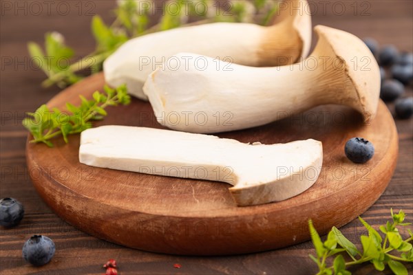 King Oyster mushrooms or Eringi (Pleurotus eryngii) on brown wooden background with blueberry, herbs and spices. Side view, selective focus