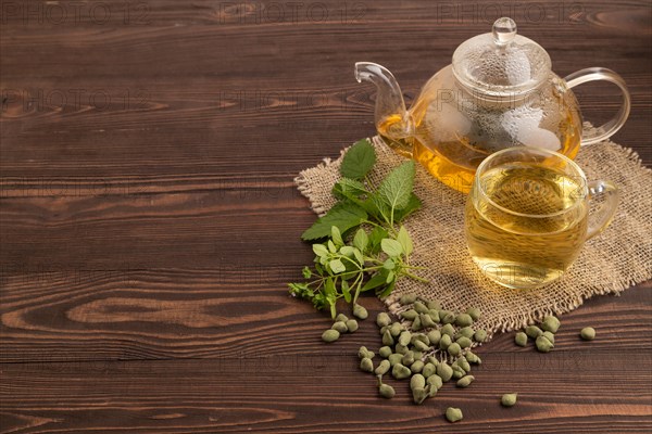 Green oolong tea with herbs in glass on brown wooden background and linen textile. Healthy drink concept. Side view, copy space