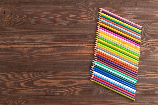 Set of watercolor pencils on brown wooden background. Top view, flat lay, copy space