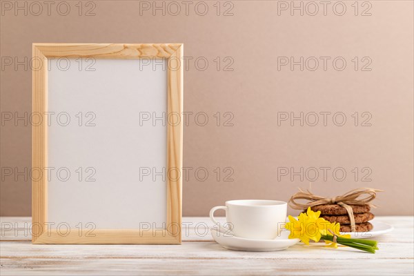 Wooden frame with oatmeal cookies yellow narcissus and coffee cup on beige pastel background. side view, copy space, still life, mockup, template, spring minimalism concept