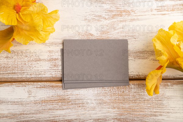 Gray business card with iris yellow flowers on white wooden background. top view, flat lay, copy space, mockup, template, spring, summer minimalism concept