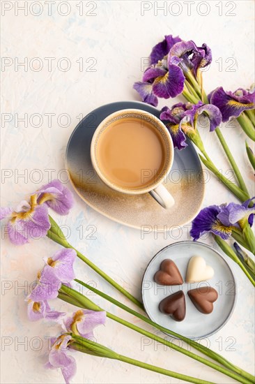 Cup of cioffee with chocolate candies and lilac iris flowers on white concrete background. top view, flat lay, close up, still life. Breakfast, morning, spring concept