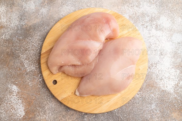 Raw chicken breast on a wooden cutting board on a brown concrete background. Top view, flat lay, close up