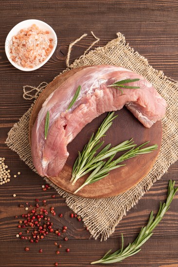 Raw pork with herbs and spices on a wooden cutting board on a brown wooden background. Top view, flat lay, close up