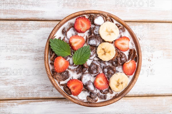 Chocolate cornflakes with milk and strawberry in wooden bowl on white wooden background. Top view, close up