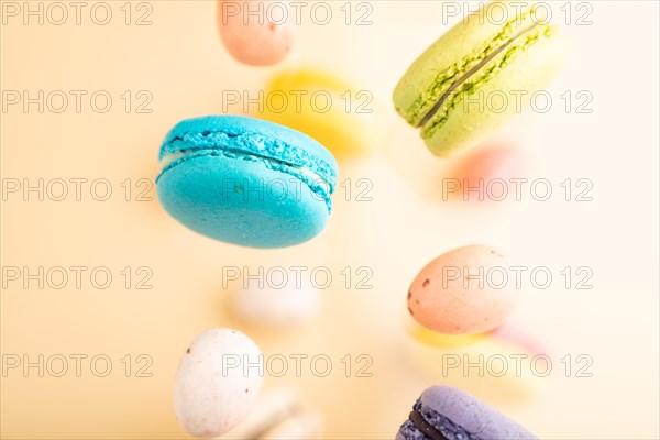 Multicolored flying macaroons and chocolate eggs frozen in the air on blurred beige background. top view, flat lay, close up. Breakfast, morning, concept