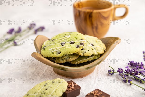 Green cookies with chocolate and mint on leaflike ceramic plate with cup of coffee on gray concrete background. side view, close up, selective focus