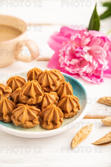 Homemade soft caramel fudge candies on blue plate and cup of coffee on gray concrete background, peony flower decoration. side view, close up, selective focus