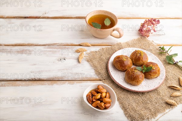 Homemade traditional turkish dessert sekerpare with almonds and honey, cup of green tea on white wooden background and linen textile. side view, copy space