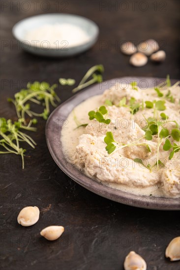 Stewed chicken fillets with coconut milk sauce and rucola microgreen on black concrete background and blue linen textile. side view, close up, selective focus