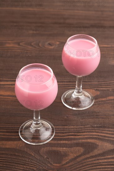 Sweet strawberry liqueur in glass on a brown wooden background. side view, close up