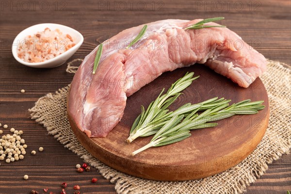 Raw pork with herbs and spices on a wooden cutting board on a brown wooden background. Side view, close up