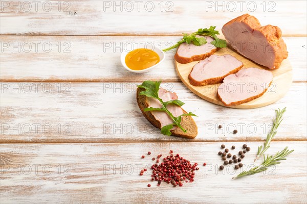 Smoked pork ham on cutting board with pepper and herbs on white wooden background. Side view, copy space