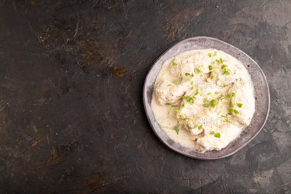 Stewed chicken fillets with coconut milk sauce and rucola microgreen on black concrete background. top view, flat lay, copy space