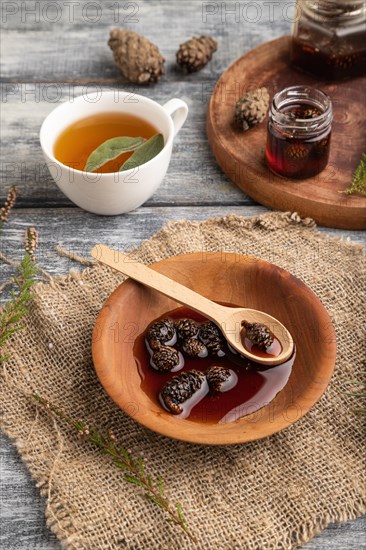 Pine cone jam with herbal tea on gray wooden background and linen textile. Side view, close up