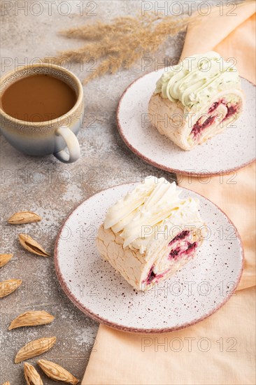 Roll biscuit cake with cream cheese and jam, cup of coffee on brown concrete background and orange linen textile. side view, close up