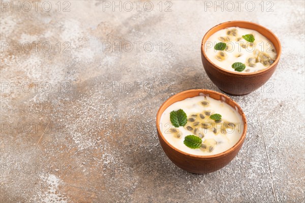 Yoghurt with granadilla and mint in clay bowl on brown concrete background. side view, copy space