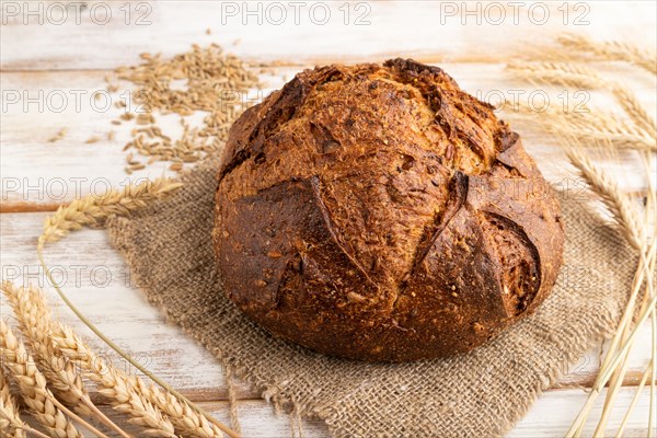Fresh homemade golden grain bread with ears of wheat and rye on white wooden background and linen textile. side view, close up
