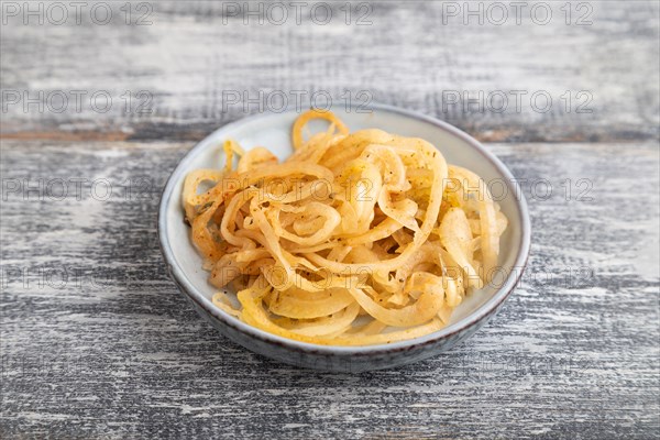 Marinated onion on a blue ceramic plate on a gray wooden background. Side view, close up