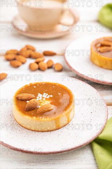 Sweet tartlets with almonds and caramel cream with cup of coffee on a white wooden background and green textile. side view, close up, selective focus