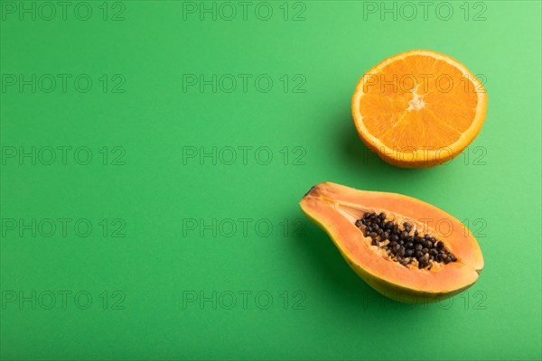 Ripe cut papaya and orange on green pastel background. Side view, copy space. Tropical, healthy food, women health concept, minimalism
