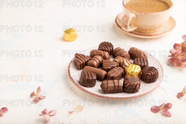Chocolate candies with cup of coffee and hydrangea flowers on a white concrete background. side view, close up