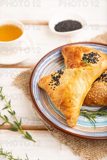 Homemade asian pastry samosa, cup of green tea on white wooden background and linen textile. side view, selective focus