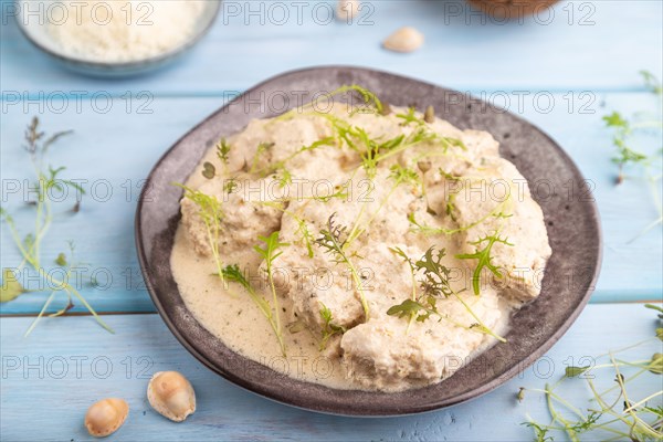 Stewed chicken fillets with coconut milk sauce and mizuna cabbage microgreen on blue wooden background. side view, close up, selective focus