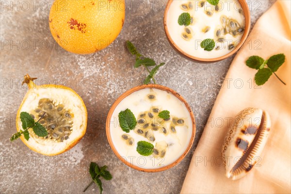 Yoghurt with granadilla and mint in clay bowl on brown concrete background and orange linen textile. top view, flat lay, close up