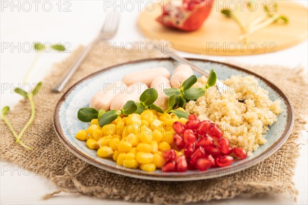 Mixed quinoa porridge, sweet corn, pomegranate seeds and small sausages on white wooden background. Side view, close up, selective focus. Food for children, healthy food concept